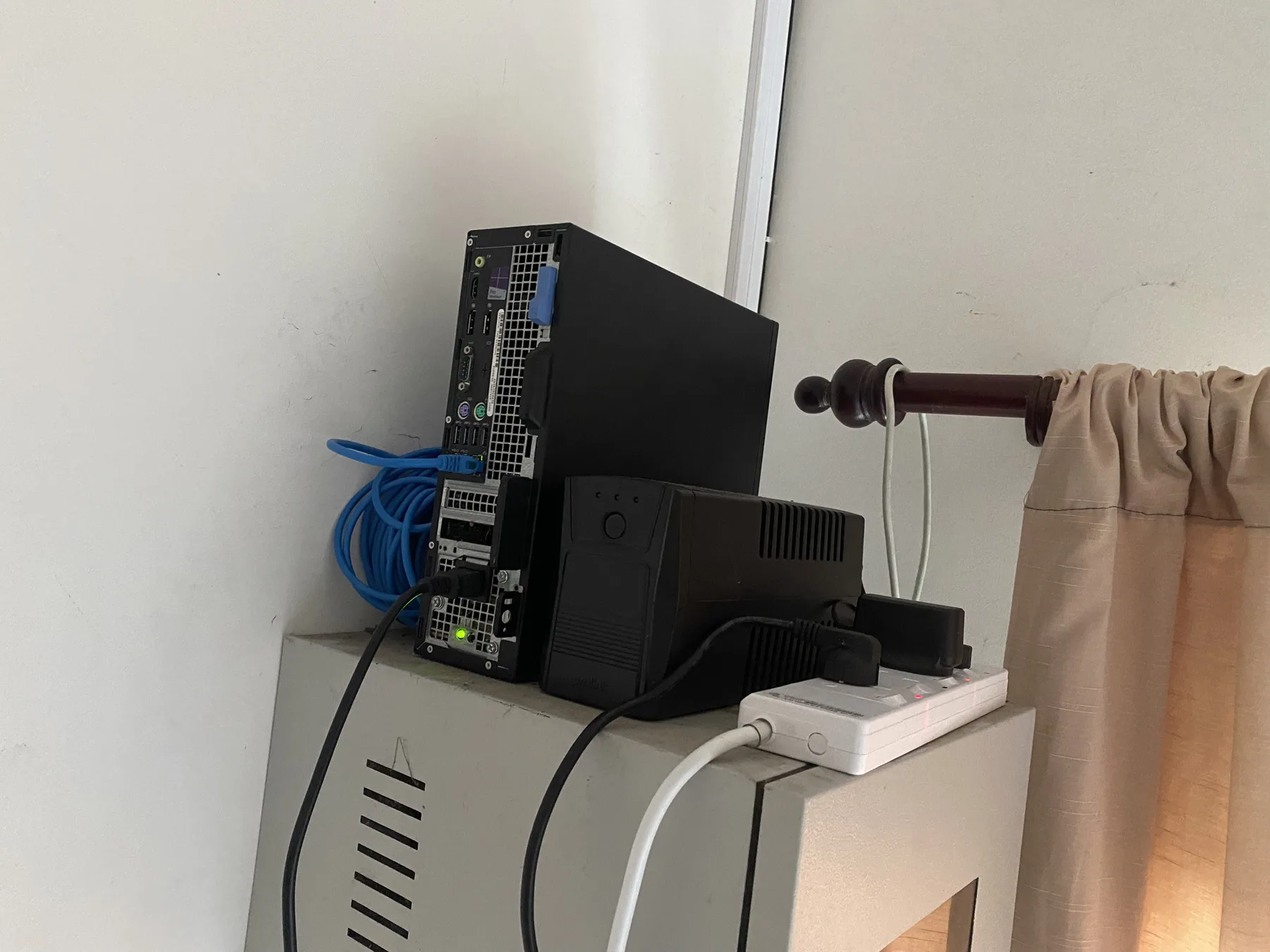 Compact home-lab server, UPS, network cable, and power hardware mounted above a metal cabinet